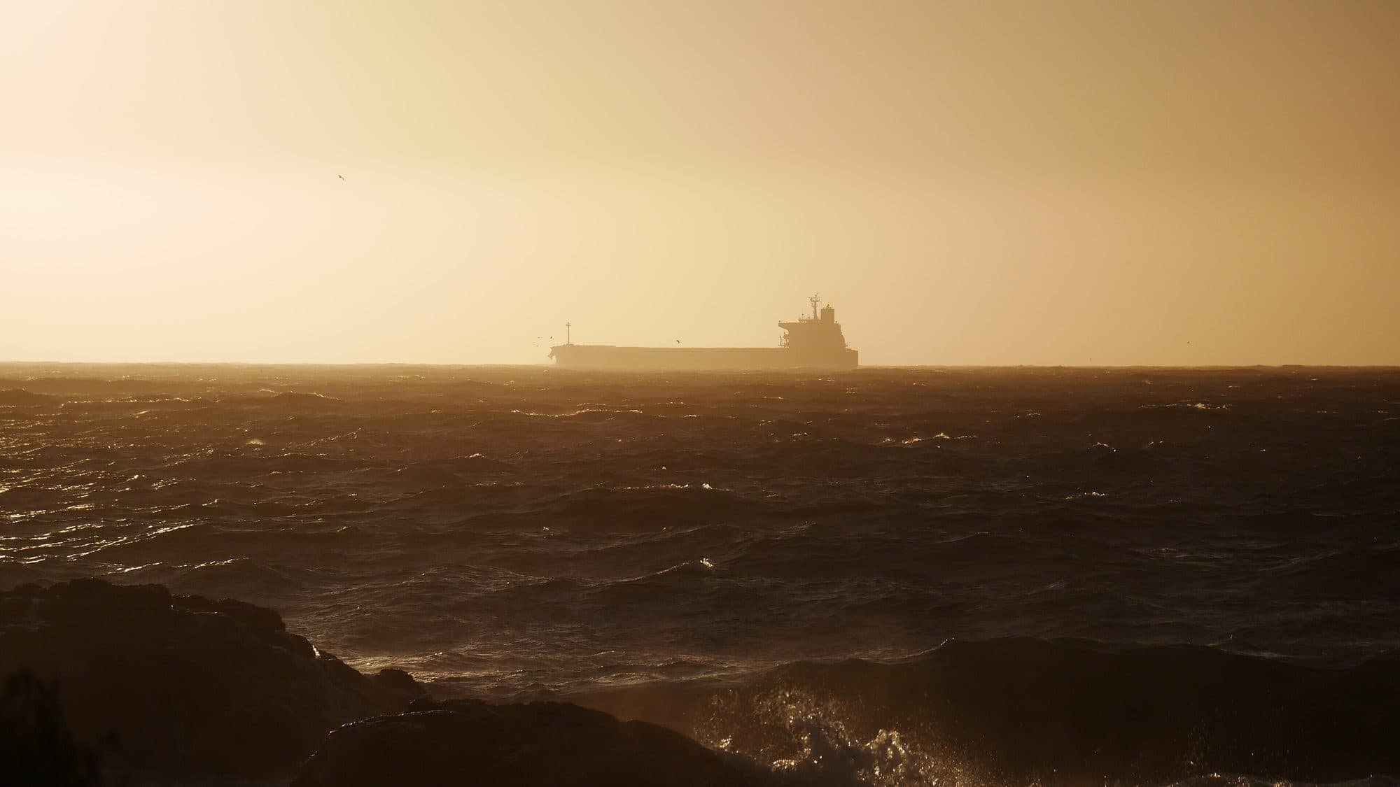 Silhouette eines großen Frachtschiffs auf rauer See in der Abenddämmerung